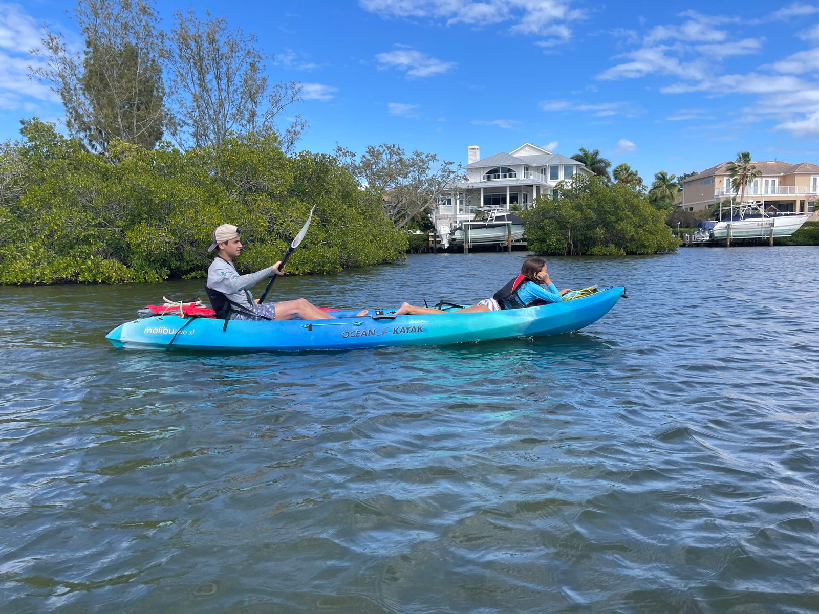 Girl laying on tandem kayak while boy paddles